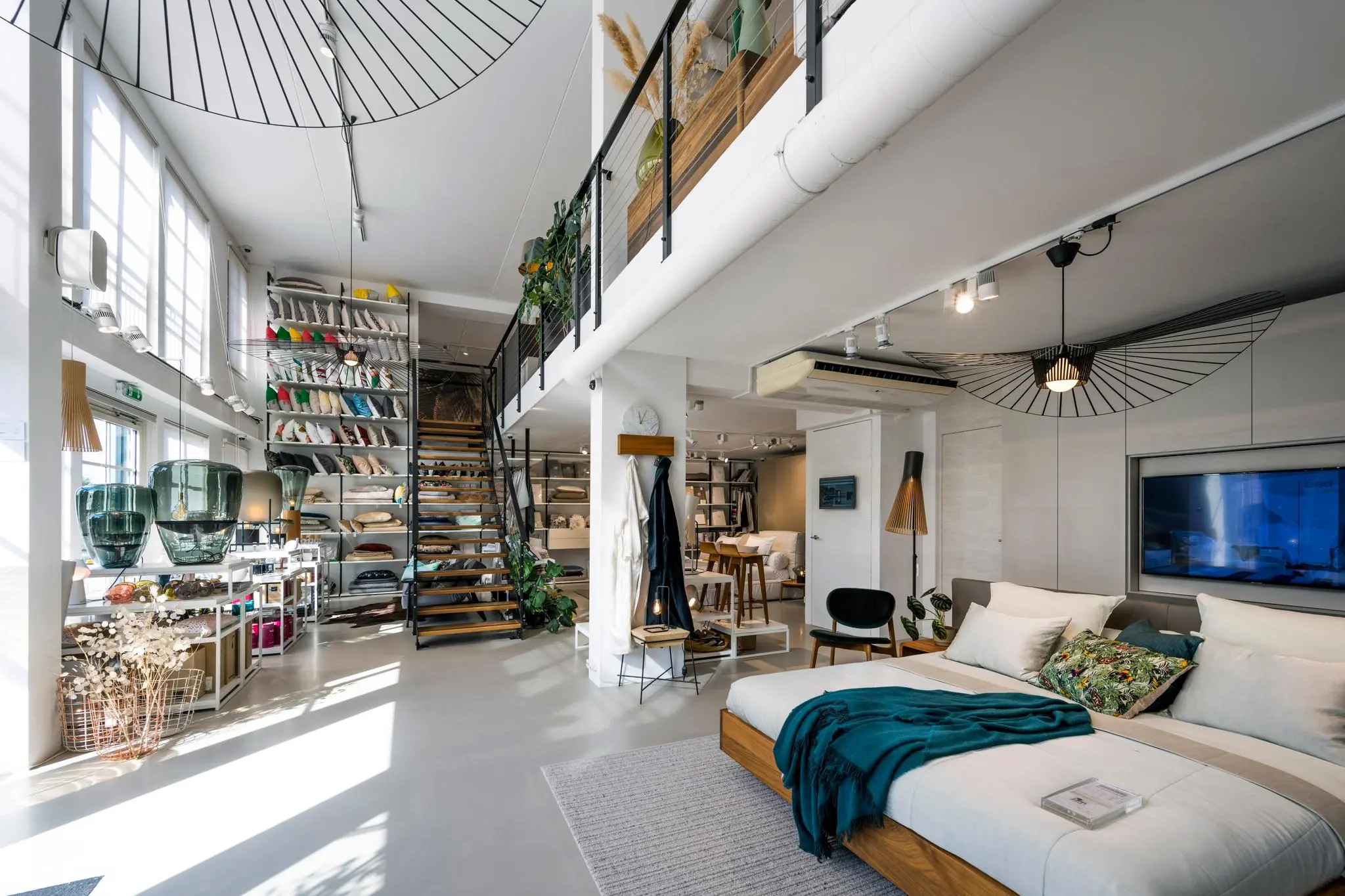 Modern ingerichte showroom aan de Oostelijke Handelskade met een bed, decoratieve kussens en een open trap naar een bovenverdieping.